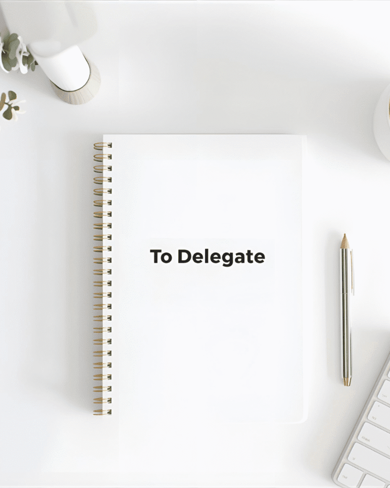 "Minimalist white desk with a 'To Delegate' notebook, pen, keyboard, and plant, symbolizing the power to delegate.