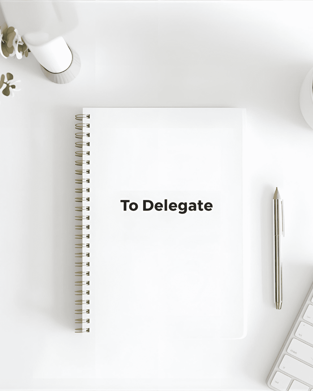 "Minimalist white desk with a 'To Delegate' notebook, pen, keyboard, and plant, symbolizing the power to delegate.