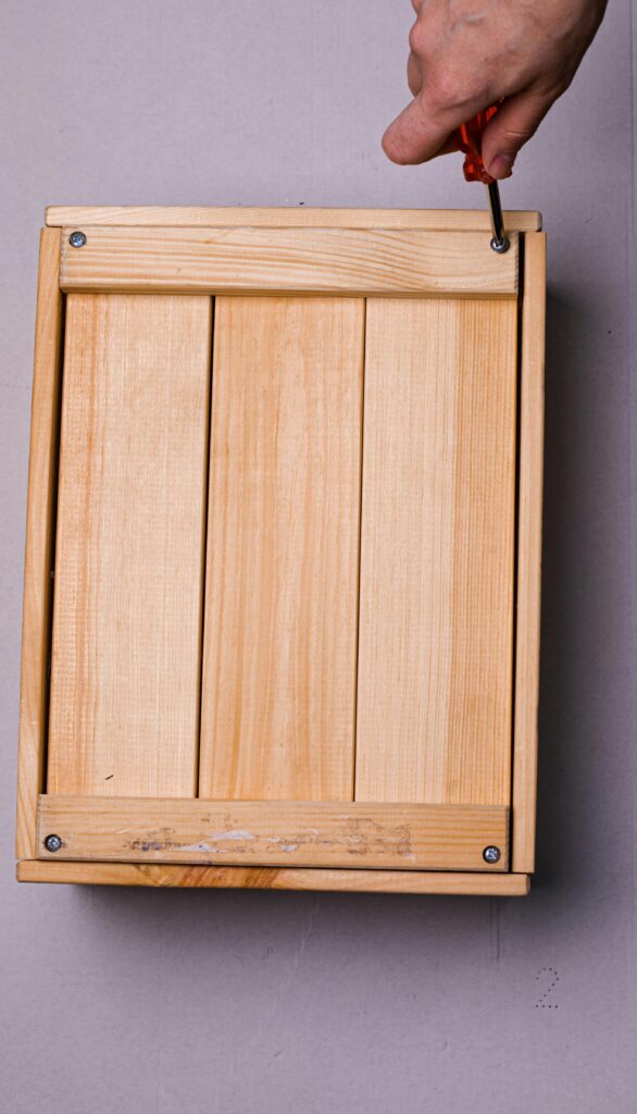 Close-up of hand using screwdriver on a wooden box. DIY carpentry concept.